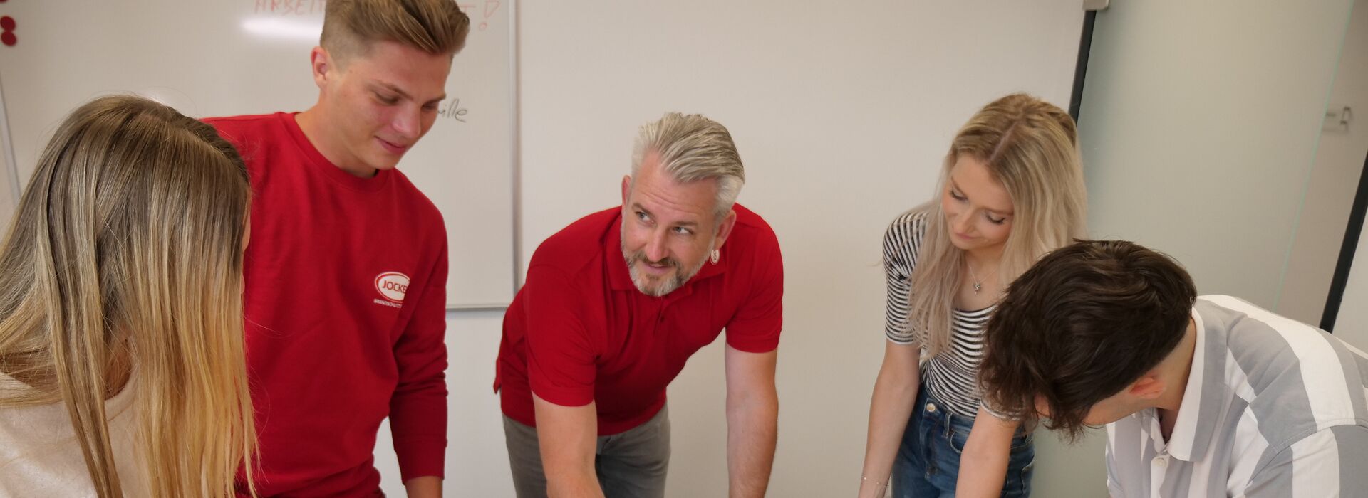 Ausbilder mit 4 Azubis um einen Schreibtisch