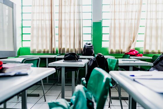 Ein Klassenzimmer mit grünen Stühlen, Tischen und Rucksäcken, beleuchtet von Tageslicht durch die Fenster.