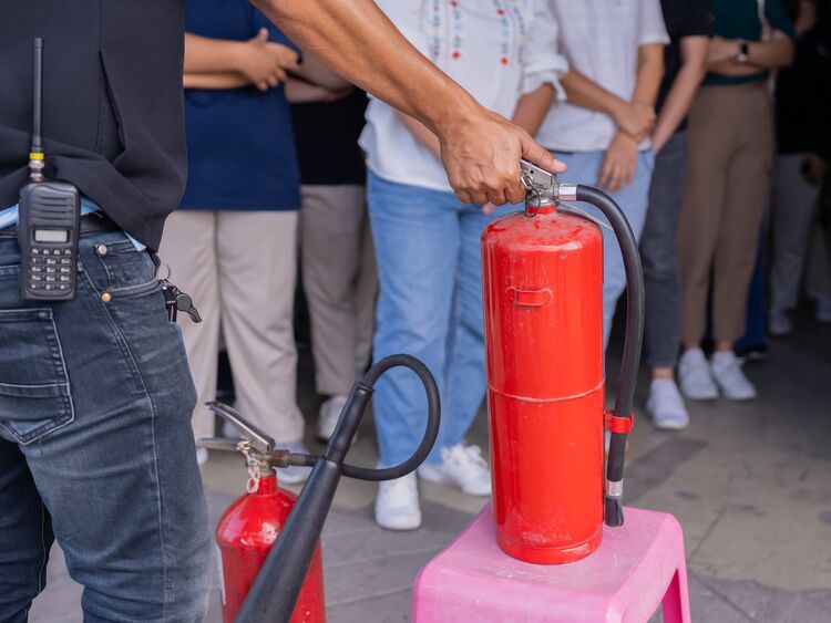 Ein Mann erklärt die Funktionsweise eines Feuerlöschers. Im Hintergrund ist eine Personengruppe zu sehen.