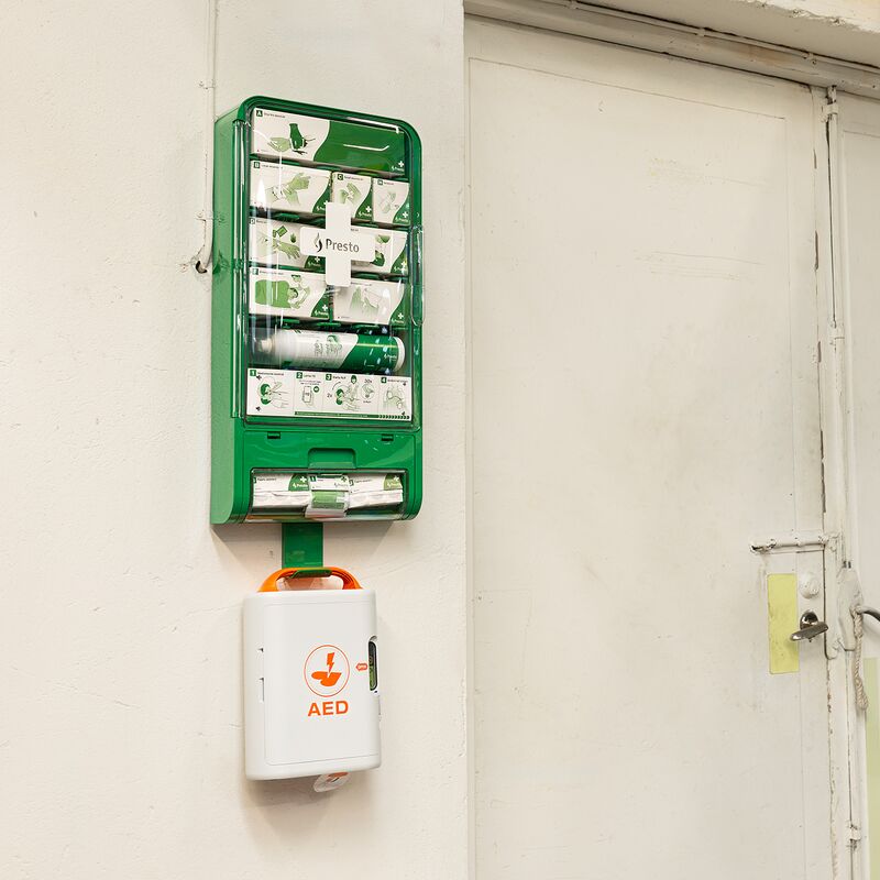 An einer Wand in einem Industribetrieb hängt eine Erste-Hilfe-Station mit AED Defibrillator