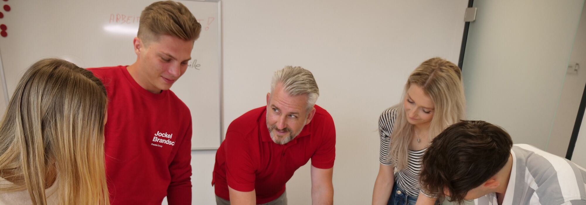 Ausbilder mit 4 Azubis um einen Schreibtisch