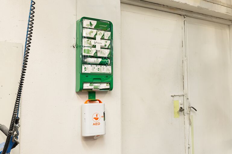 An einer Wand in einem Industribetrieb hängt eine Erste-Hilfe-Station mit AED Defibrillator