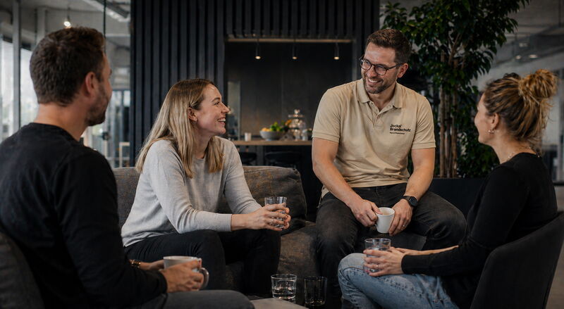 Die Mitarbeiter unterhalten sich in einer Lounge. Die Atmosphäre ist entspannt.